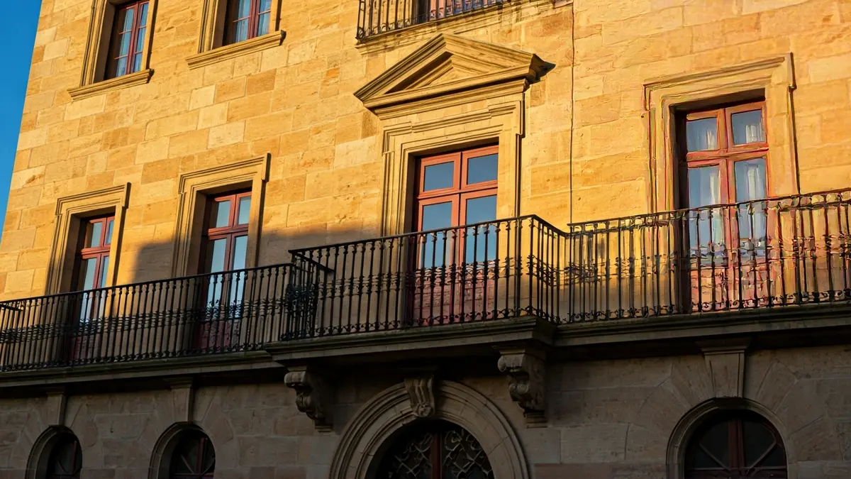 Fachada de un ayuntamiento de piedra con balcón y barandillas de hierro