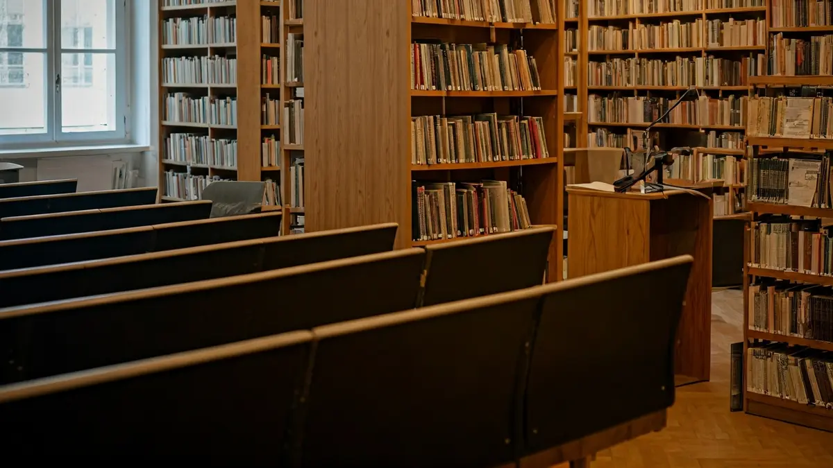 Imaxe xenérica dunha sala de presentacións ou biblioteca, con estantes de madeira e un micrófono.