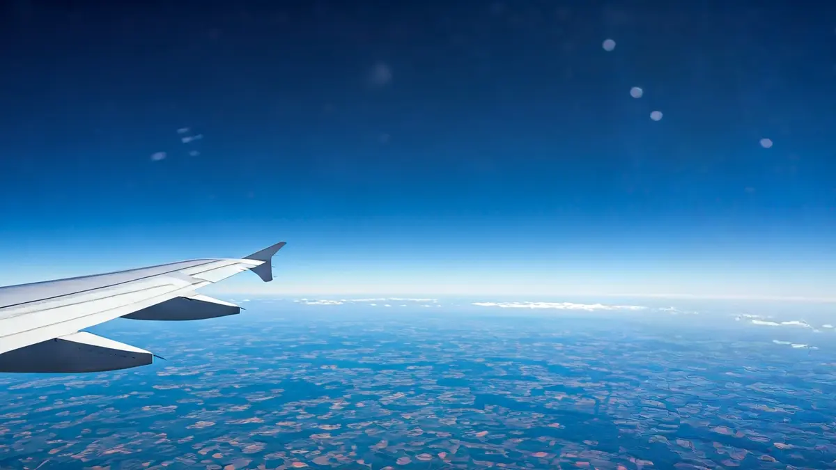 Imaxe xenérica dunha á de avión en voo, con nubes e terra ao fondo.
