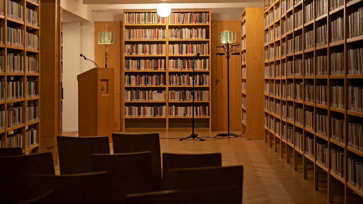 Imaxe xenérica dunha biblioteca acolladora con estantes de madeira e un podio con micrófono.