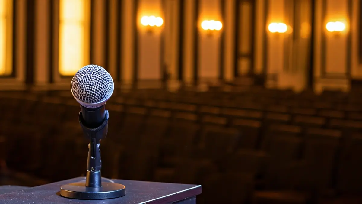 Imagen genérica de un micrófono en un escenario, con sillas vacías al fondo.