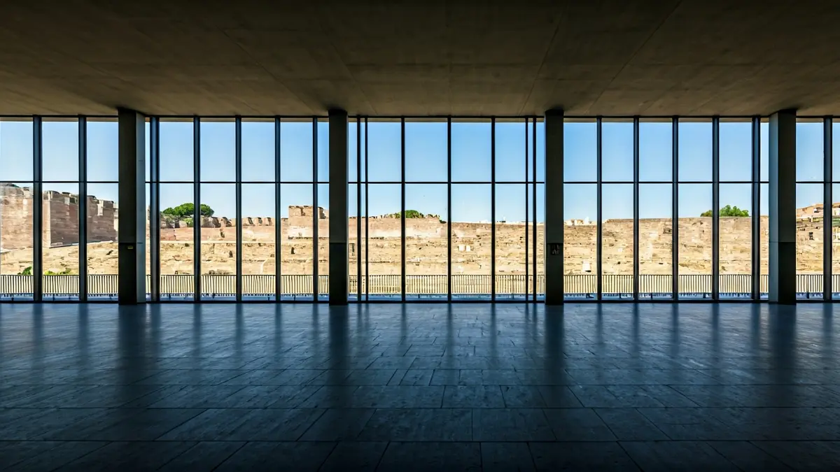 Imaxe dunha estación de autobuses moderna coa muralla romana ao fondo.