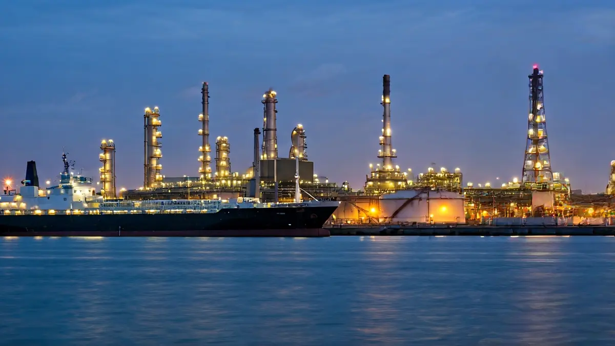 Refinería de petróleo ao anoitecer, con tanques de almacenamento e barcos.
