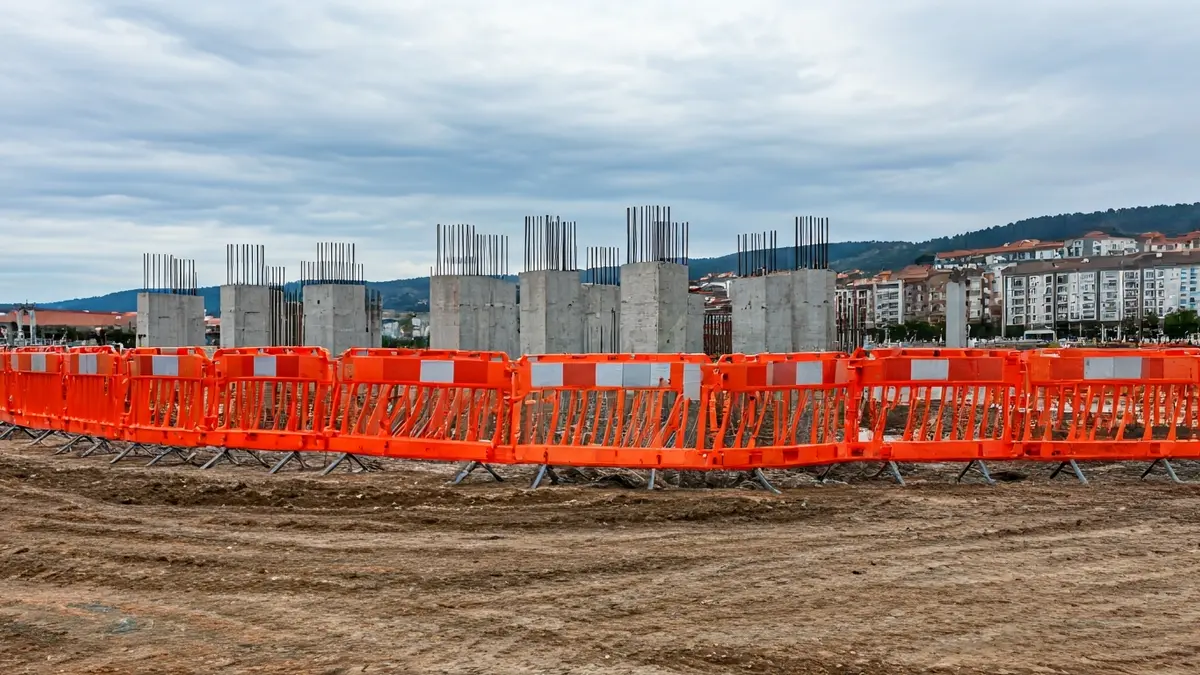 Imaxe dunha obra en construción con barreiras de seguridade laranxas.