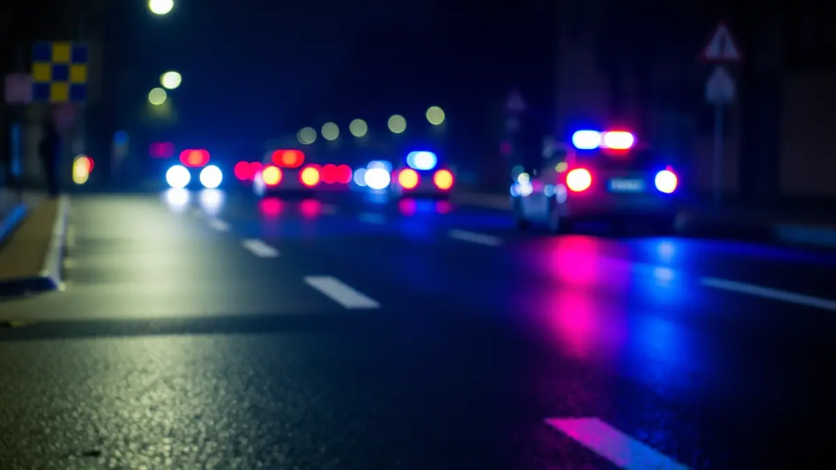 Imaxe xenérica de luces de emerxencia reflectíndose sobre asfalto mollado pola noite.