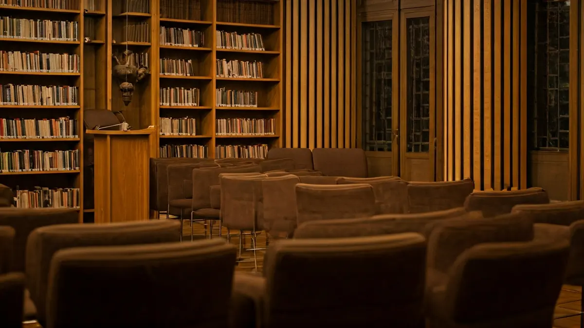 Imaxe xenérica dunha sala de actos ou biblioteca, con micrófono e cadeiras baleiras.