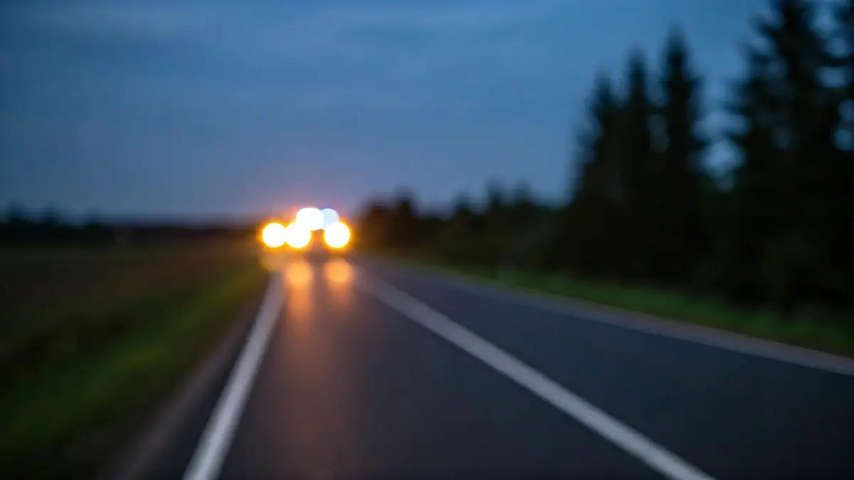 Imaxe xenérica dunha estrada rural ao anoitecer con luces de emerxencia ao lonxe.