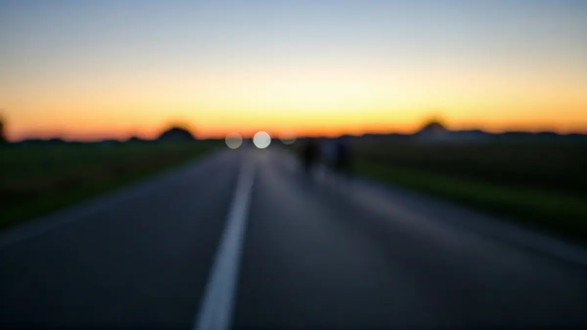 Imagen genérica de una carretera rural al amanecer, con luces de emergencia a lo lejos.