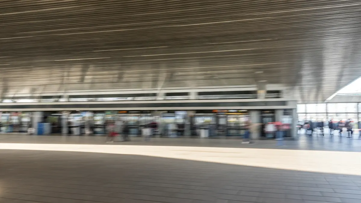 Imaxe xenérica dunha estación de autobuses moderna, con persoas borrosas e luz natural.