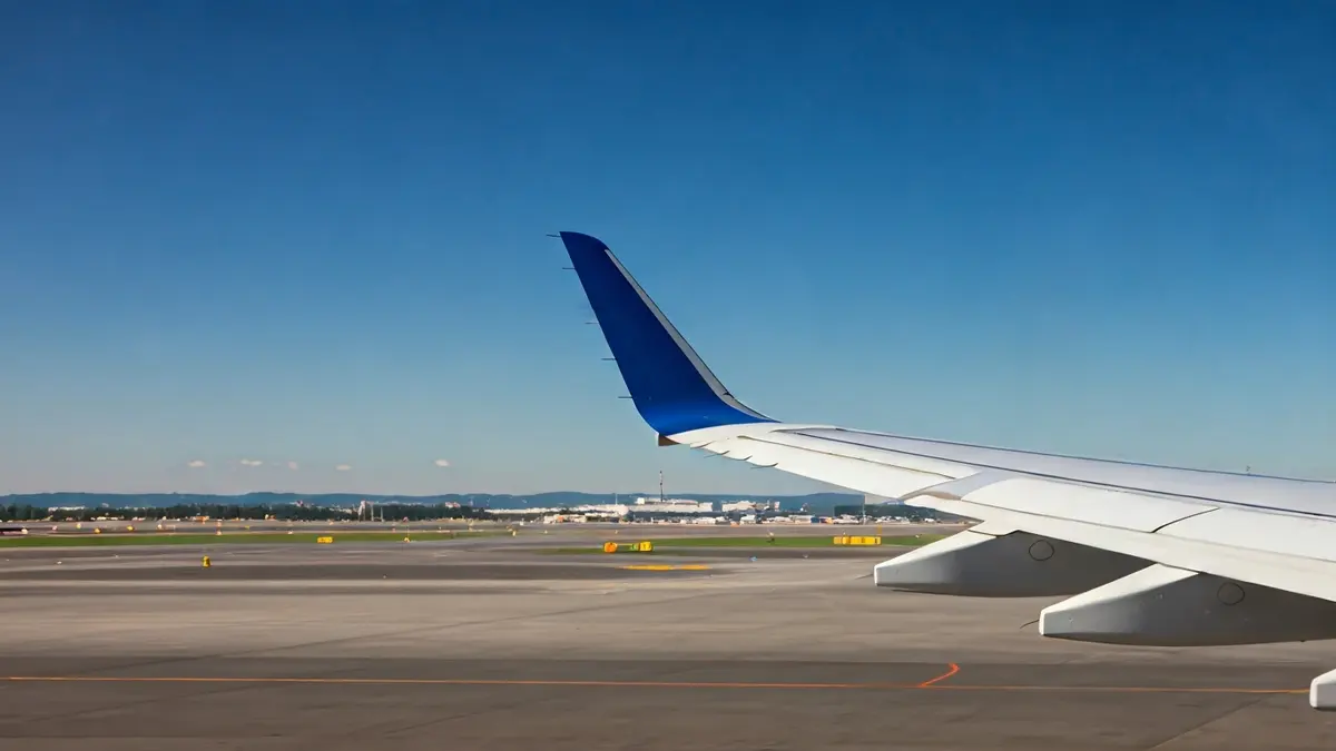 Imaxe xenérica dunha á de avión no ceo, con luces de pista borrosas ao fondo.