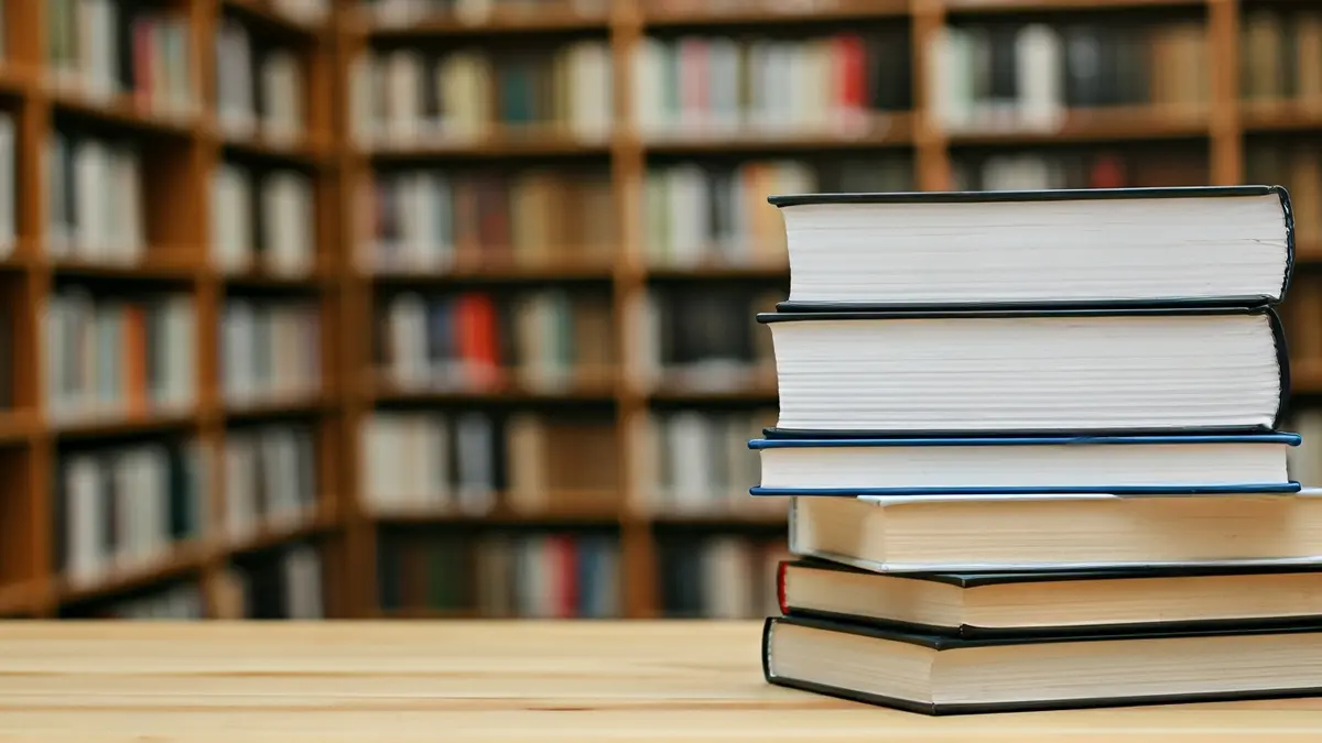 Imagen genérica de libros en una mesa, con estantes de biblioteca al fondo.