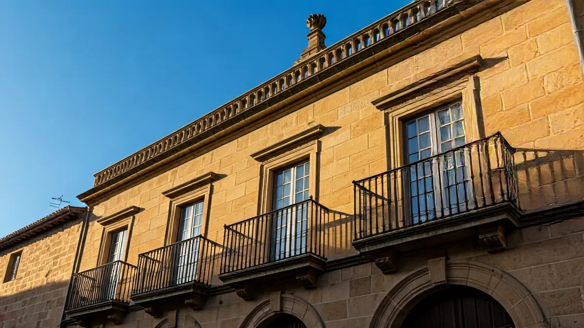 Imaxe da fachada dun concello de pedra con balcón e varandas de ferro.