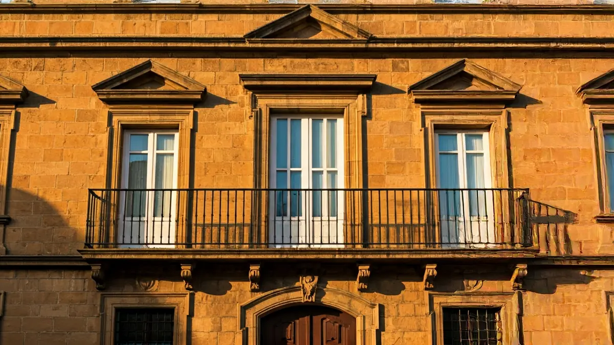 Imaxe da fachada dun concello de pedra con balcón e varandas de ferro