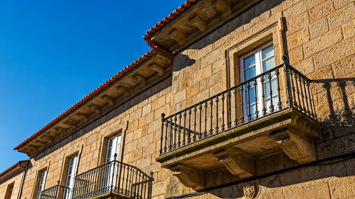 Imaxe da fachada dun concello galego, con balcón e varandas de ferro, baixo o sol da tarde.