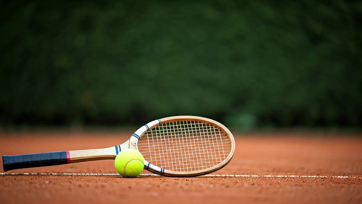 Imagen genérica de una raqueta de tenis y una pelota en una pista de tierra batida.