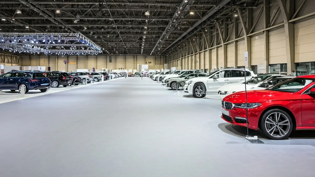 Imagen genérica de un salón de exposiciones de vehículos vacío, con coches modernos en fila y carteles de 'en venta'.