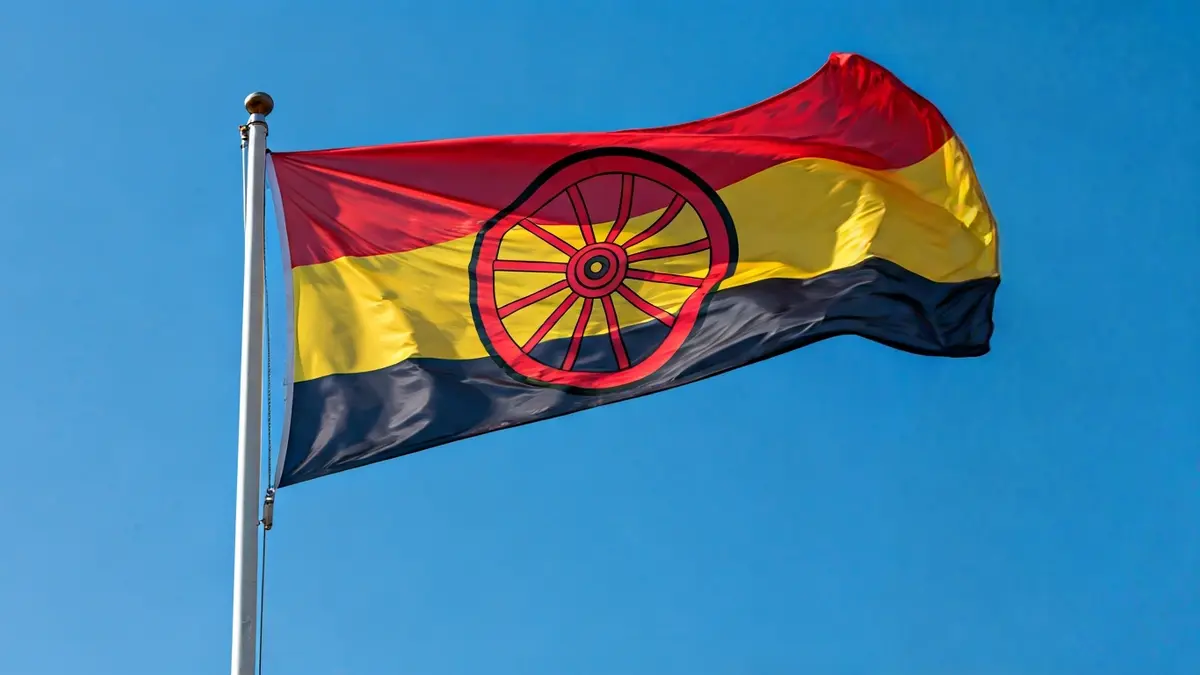 Bandera del pueblo gitano donde el azul representa el cielo y el verde la tierra, con una rueda de carreta roja en el centro.