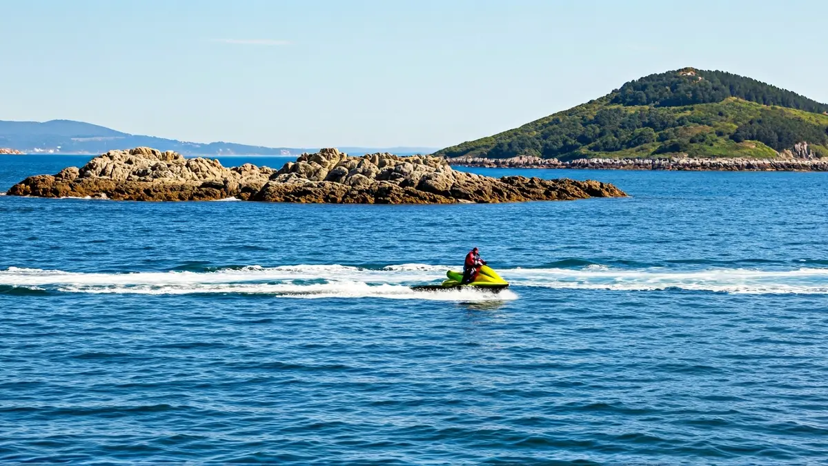 Imaxe dunha moto acuática rescatando unha persoa preto dunha illa rochosa en augas pouco profundas.