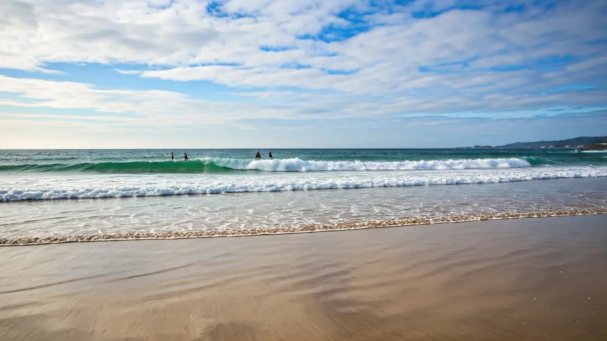 Imagen de una playa en Galicia con tablas de surf a lo lejos.
