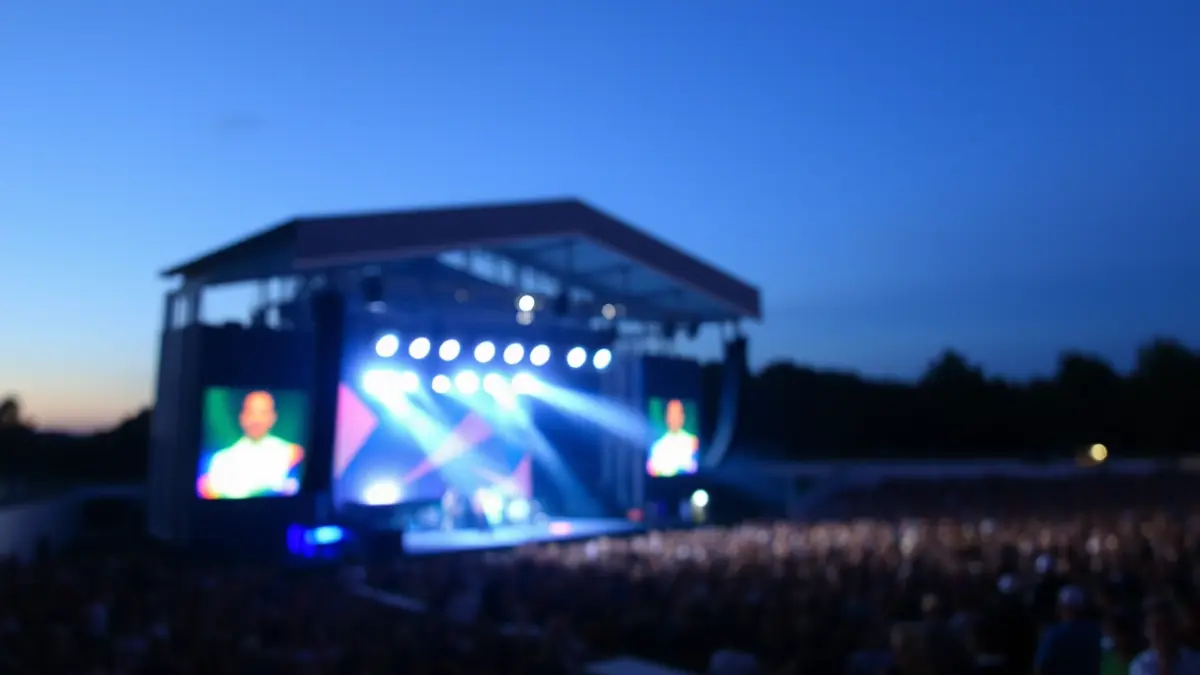 Imaxe xenérica dun concerto ao aire libre con luces brillantes e unha multitude difuminada.