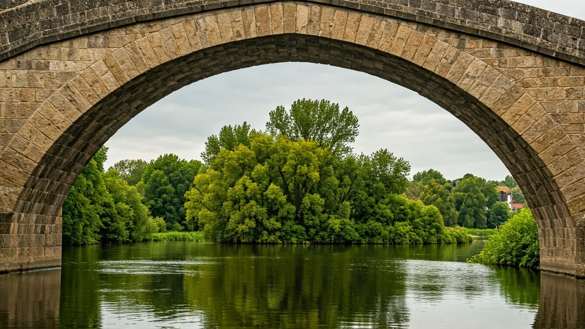 Imaxe dunha ponte de pedra antiga sobre un río, con vexetación verde nas beiras.