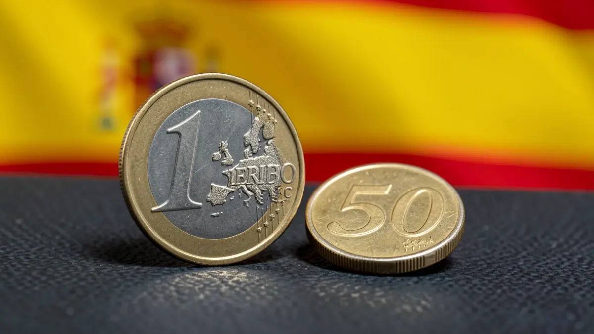 Imaxe xenérica de moedas de euro sobre un fondo difuminado da bandeira española.