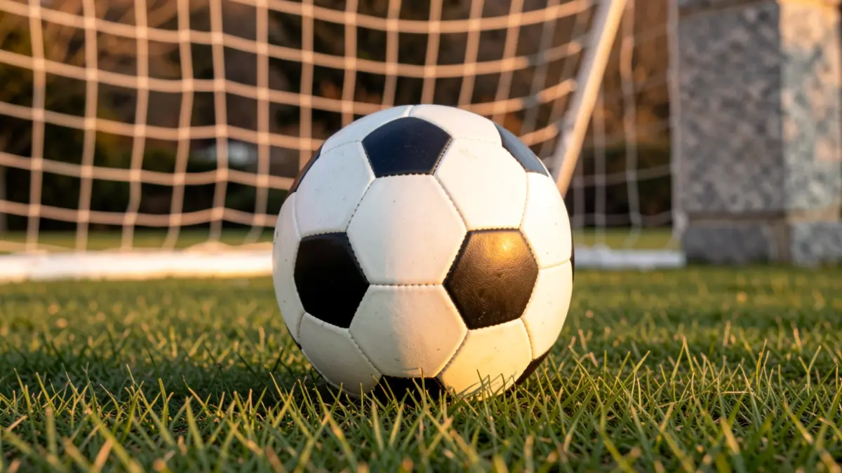 Imaxe xenérica dun balón de fútbol sobre herba con rede de fondo.