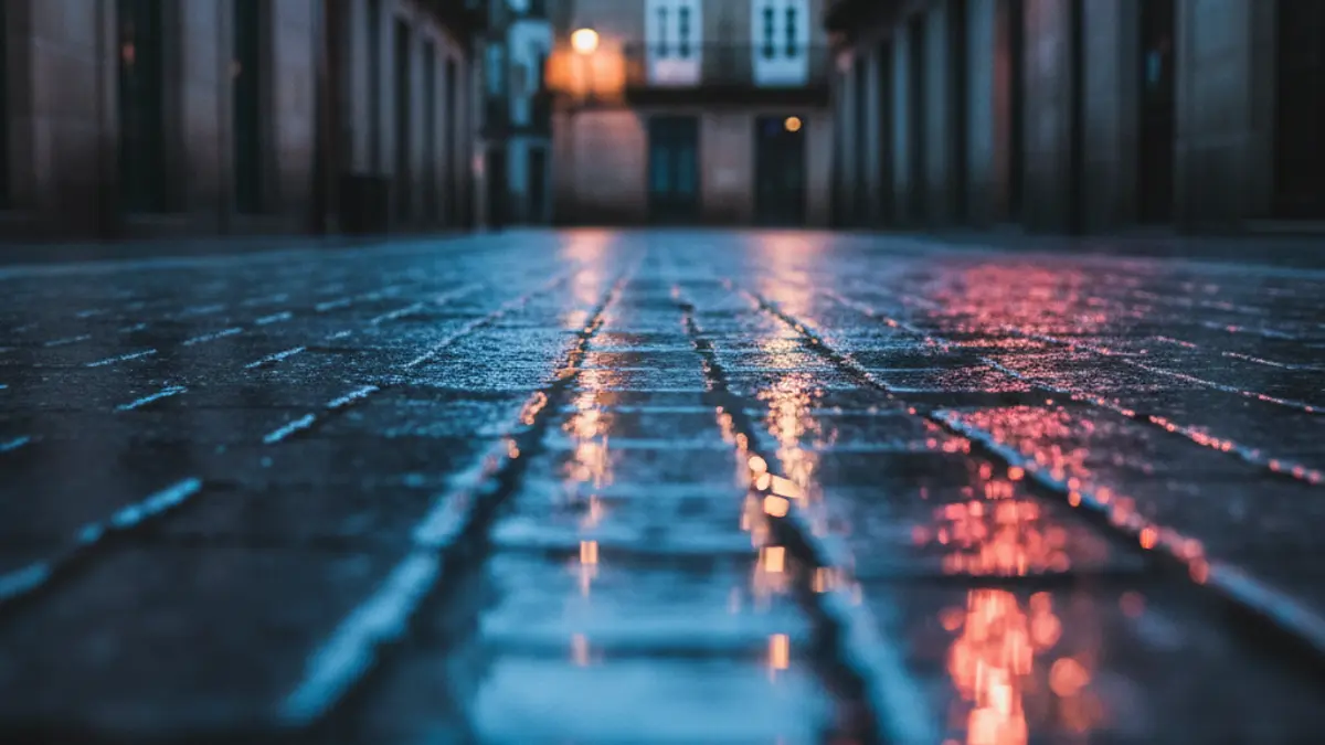 Imaxe xenérica de luces de emerxencia reflectíndose sobre asfalto mollado pola noite.