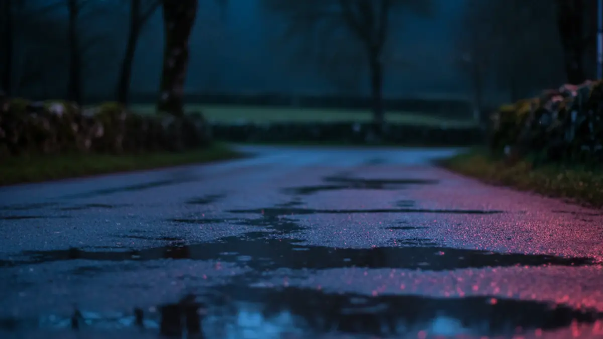 Imaxe xenérica de luces de emerxencia reflectíndose sobre asfalto mollado nunha contorna rural galega.