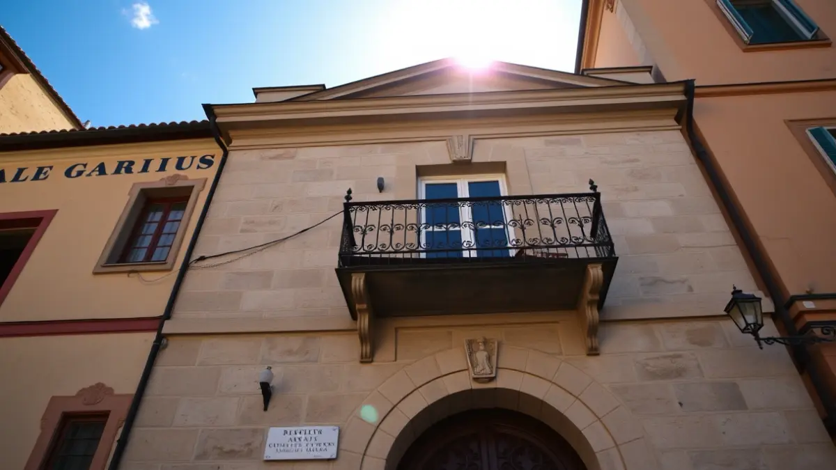 Fachada dun concello galego con balcón de ferro forxado e luz solar.