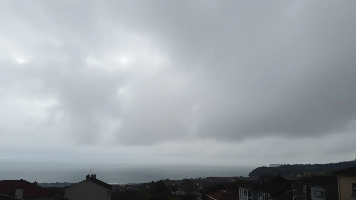 Imagen genérica de un cielo nublado con nubes altas sobre un pueblo costero gallego, con lluvia ligera y calles mojadas.