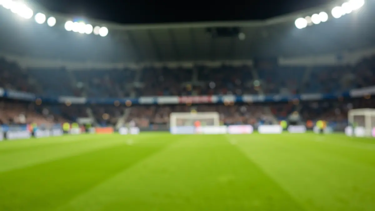 Imaxe xenérica dun estadio de fútbol baleiro con herba verde e as luces acendidas.