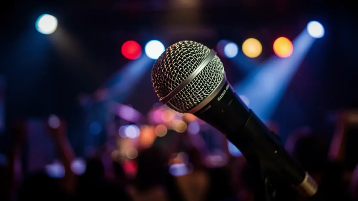 Imagen genérica de un micrófono en un escenario con luces de concierto desenfocadas.