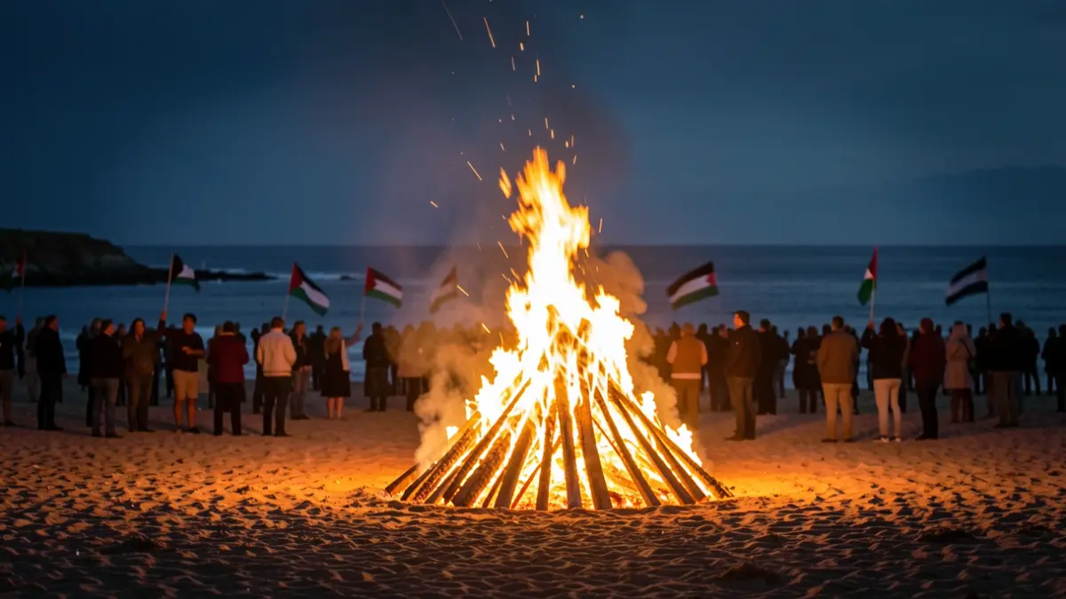 Imaxe xenérica dunha fogueira de San Xoán nunha praia con xente e bandeiras palestinas.