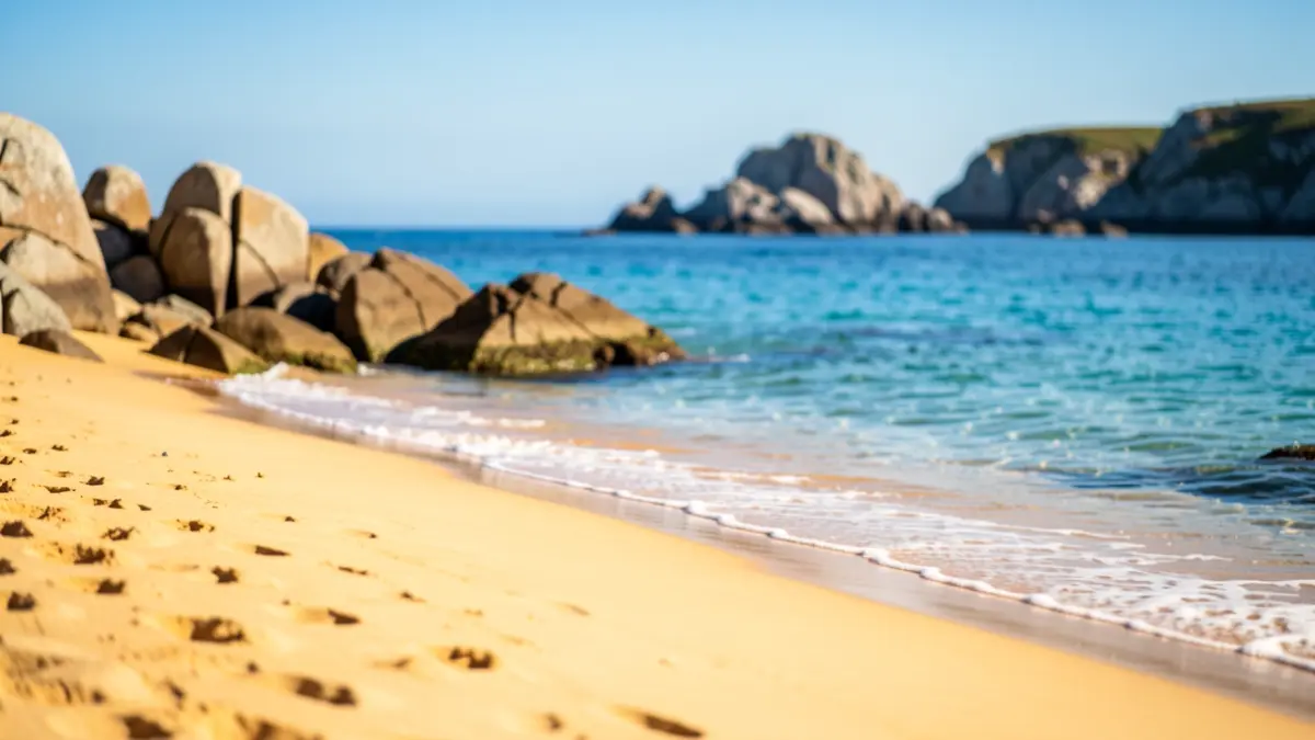 Imaxe xenérica dunha praia galega con area dourada e auga azul.