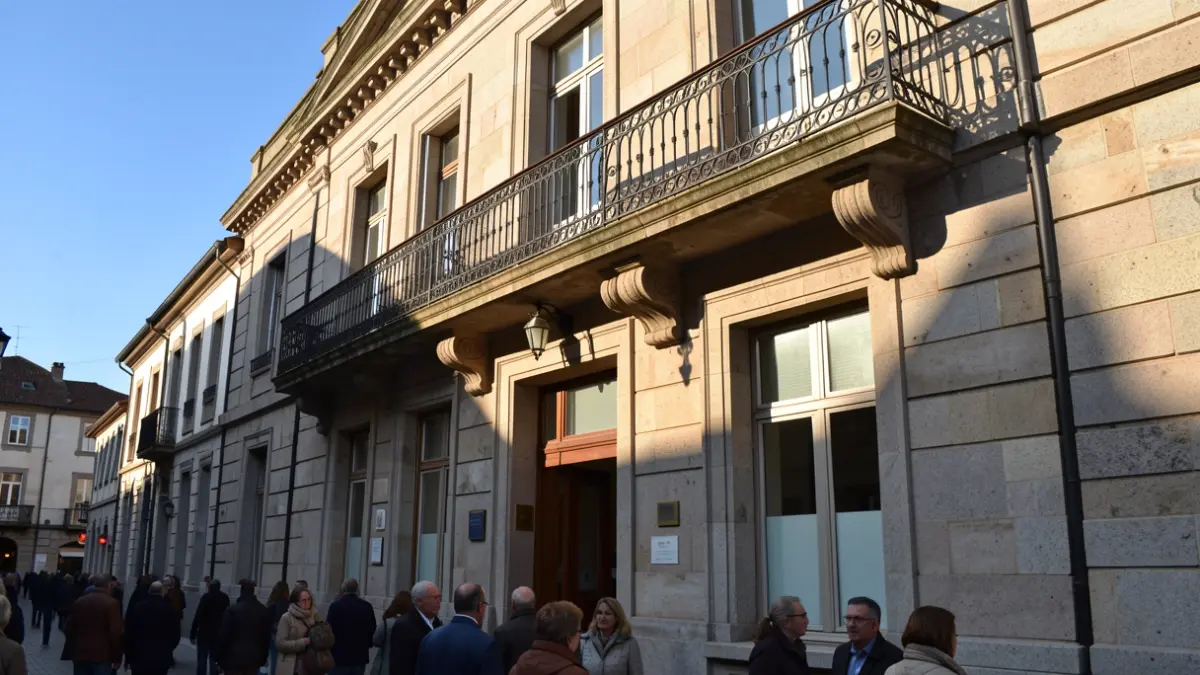 Imaxe xenérica dun concello galego de granito con balcón de ferro e luz solar.