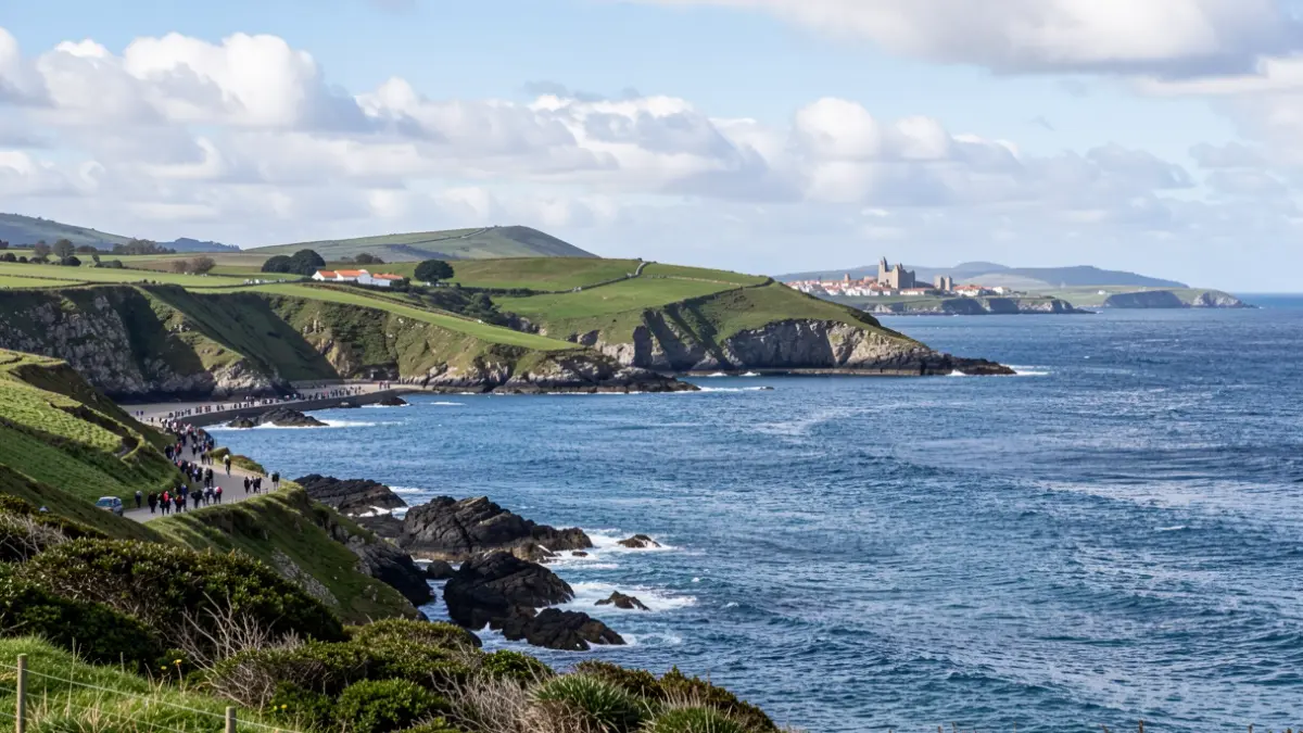 Imaxe xenérica da costa das Rías Baixas en Galicia, con outeiros verdes e o mar azul baixo un ceo con nubes.