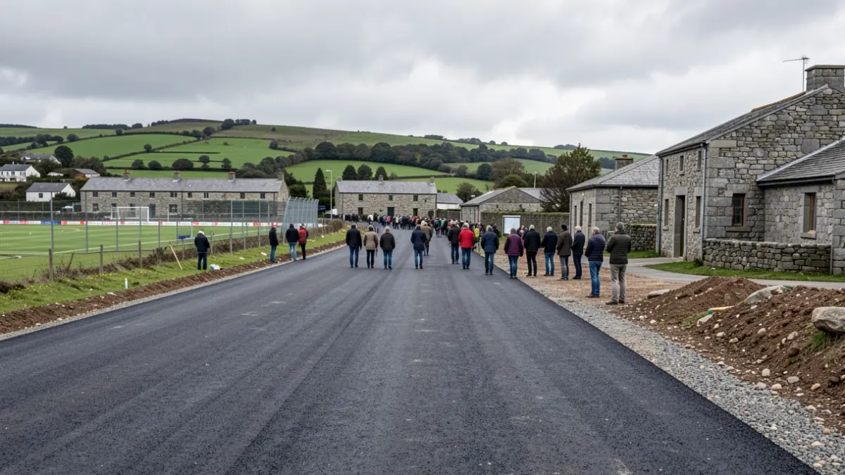 Imaxe xenérica de construción dunha estrada de asfalto nunha contorna rural galega con edificios de pedra e outeiros verdes.