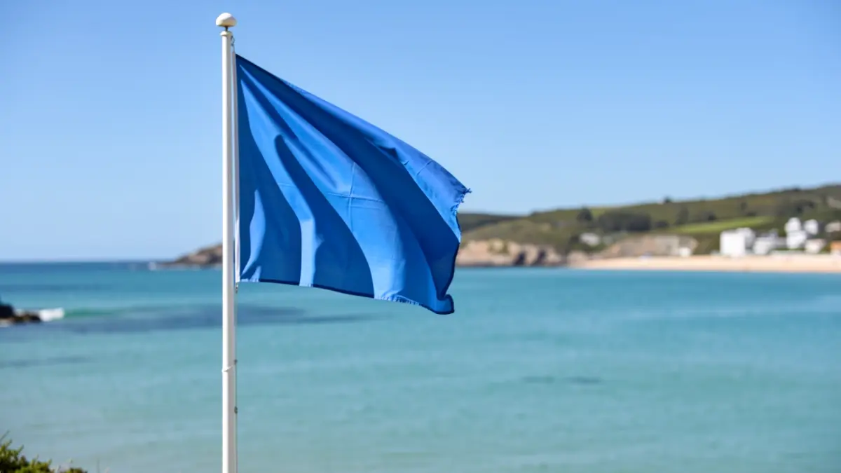 Imaxe xenérica dunha praia galega con bandeira azul ondeando.