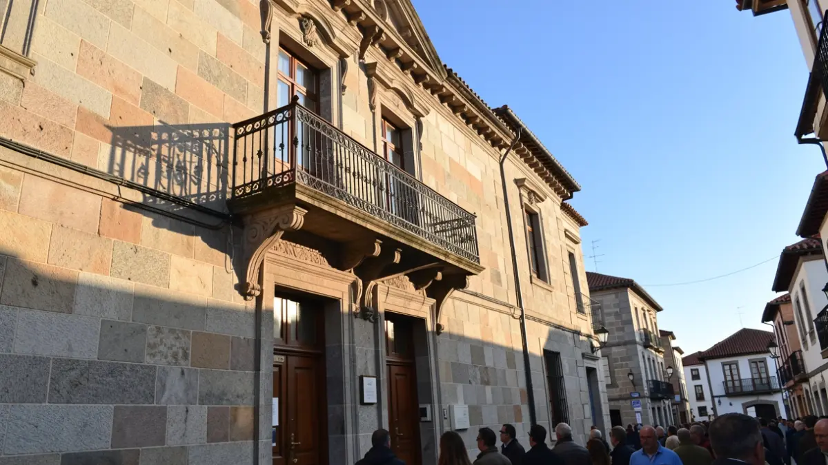 Imaxe xenérica dun concello galego de pedra con balcón e raís de ferro, á luz do sol da tarde.
