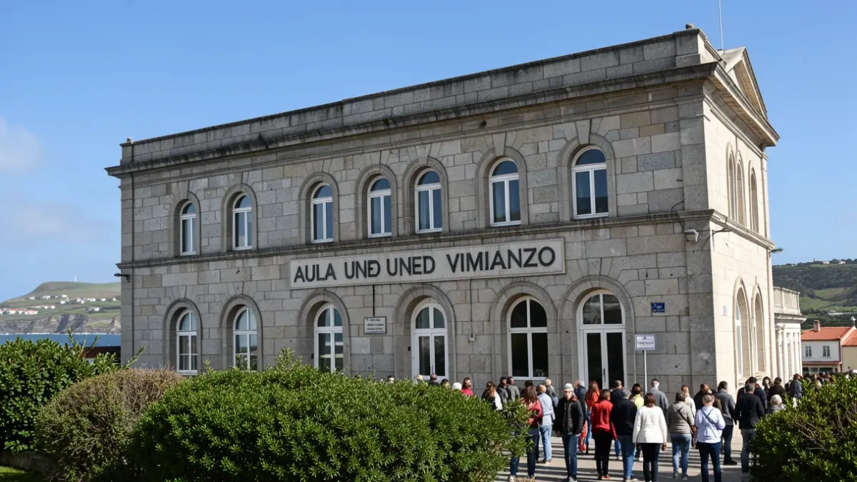 Fachada dun edificio de granito con cartel 'AULA UNED VIMIANZO' e contorna verde.